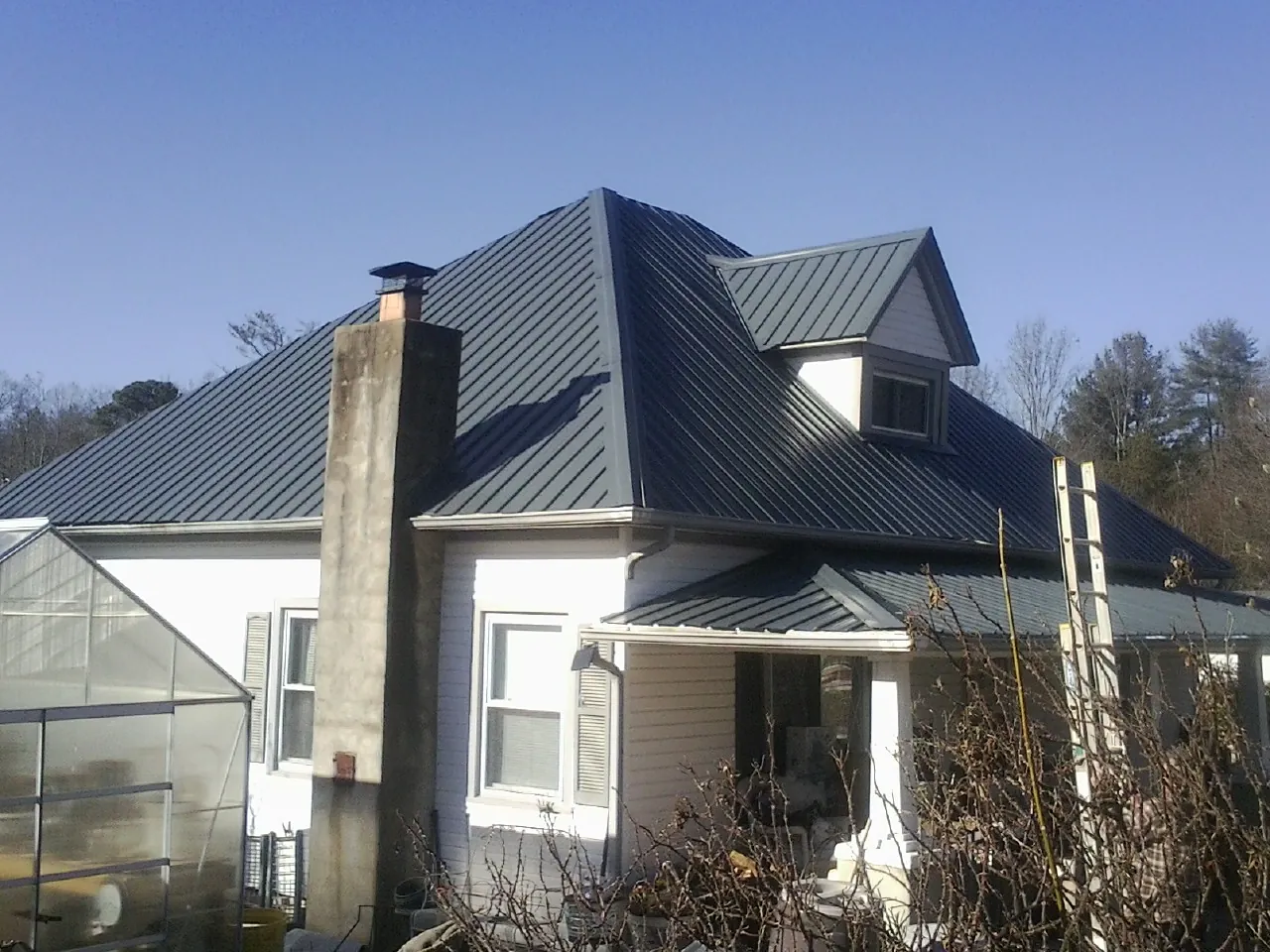 Dark blue standing seam metal roof on a white farmhouse with dormer — Slate & Tile Roof Repair by Roofing Brothers in Igo