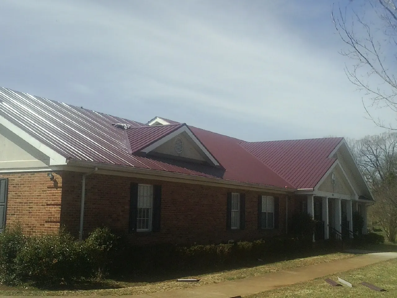 Red metal roof with gabled entries on a long brick building, from a Hail Damage Roof Repair job in Igo
