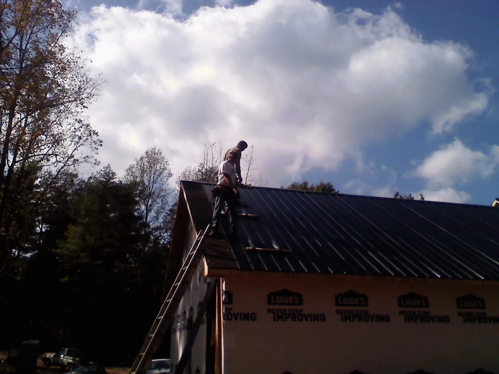 Roofer fastening dark metal panels high against a cloudy sky, from a Roof Inspection job in Igo